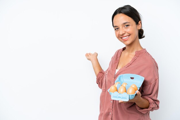 Young hispanic woman holding eggs isolated on white background extending hands to the side for inviting to come