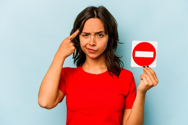 Young hispanic woman holding a forbidden sign isolated on blue\
background