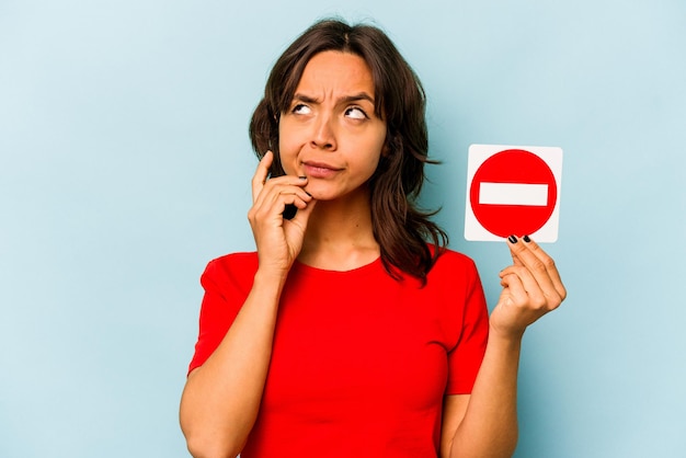 Young hispanic woman holding a forbidden sign isolated on blue\
background