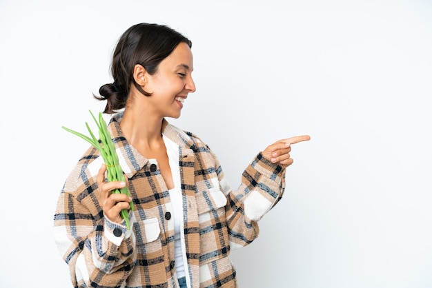 Молодая латиноамериканка держит зеленую фасоль на белом фоне, указывая пальцем в сторону