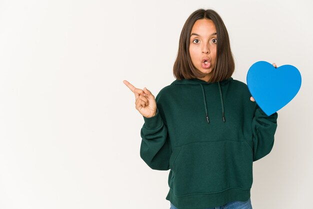 Young hispanic woman holding a heart shape pointing to the side