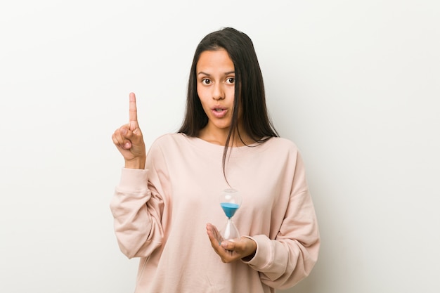 Young hispanic woman holding an hourglass having some great idea, concept of creativity.