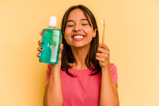 Young hispanic woman holding mouthwash isolated on yellow background