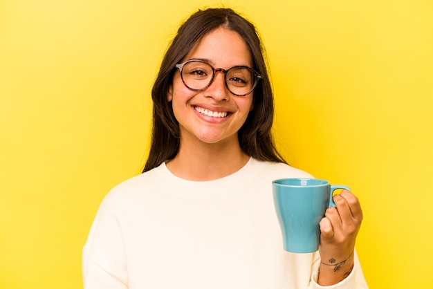 Young hispanic woman holding a mug isolated on yellow background