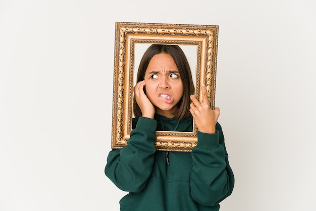 Young hispanic woman holding an old frame covering ears with hands.