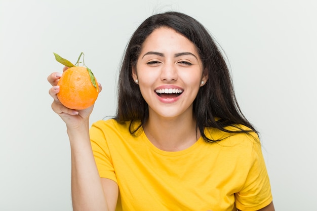 Young hispanic woman holding an orange happy, smiling and cheerful.