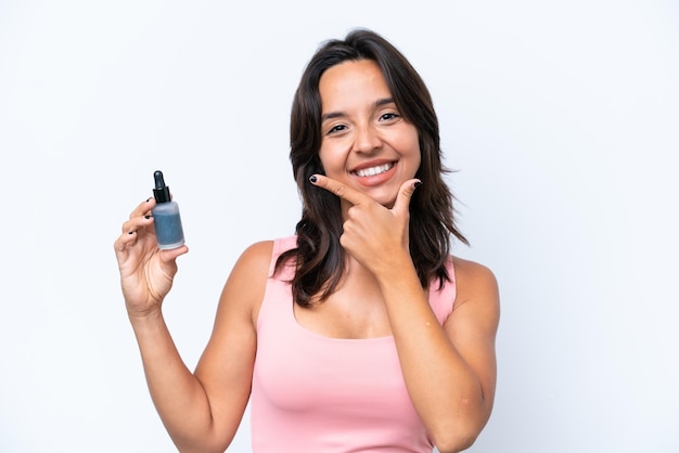 Young hispanic woman holding serum isolated on white background happy and smiling