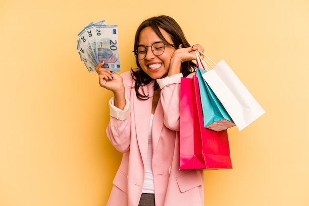 Young hispanic woman holding shopping bag isolated on yellow background