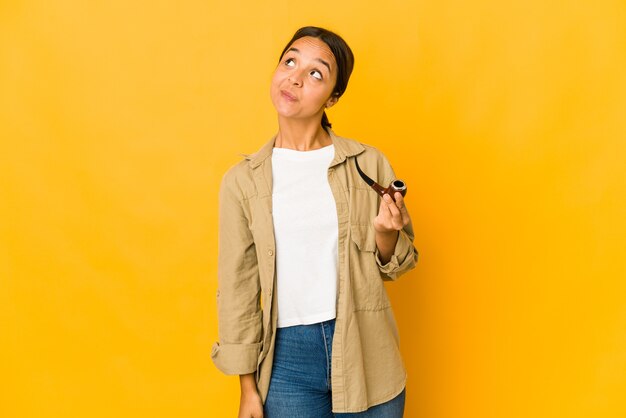 Young hispanic woman holding a smoking pipe dreaming of achieving goals and purposes