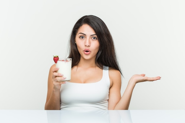 Young hispanic woman holding a smoothie young hispanic woman holding an avocado toast impressed holding copy space on palm.< mixto >