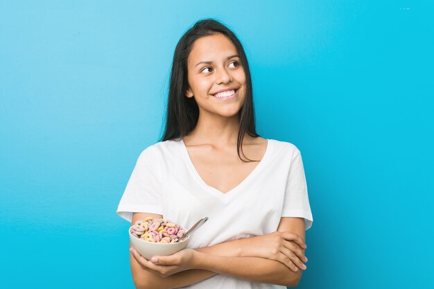 Young hispanic woman holding a sugar cereal bowl smiling confident with crossed arms.