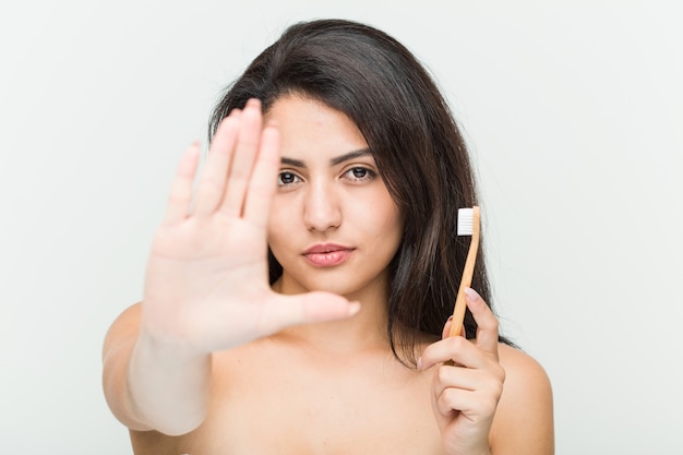 Молодая испанская женщина держа зубную щетку стоя при протягиванный знак стопа показа руки, предотвращая вас.