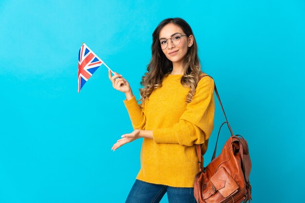 Young hispanic woman holding an United Kingdom flag on blue extending hands to the side for inviting to come