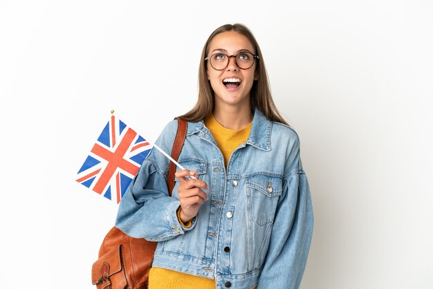 Young hispanic woman holding an United Kingdom flag over isolated white background looking up and with surprised expression