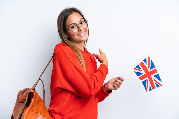 Young hispanic woman holding an United Kingdom flag isolated on white background pointing back