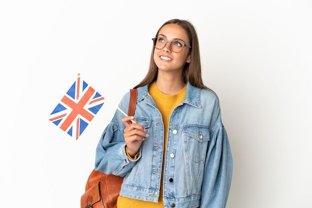 Young hispanic woman holding an United Kingdom flag over isolated white background thinking an idea while looking up