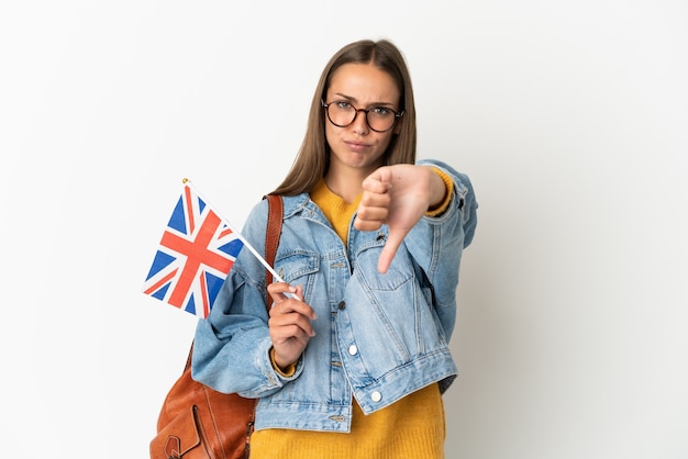 Young hispanic woman holding an United Kingdom flag over isolated white wall showing thumb down with negative expression