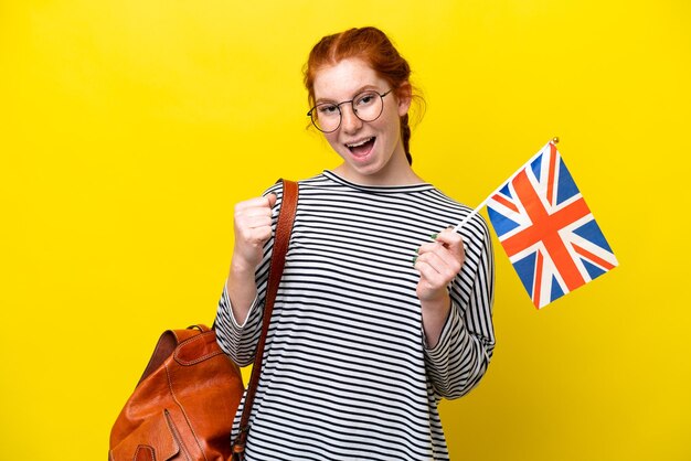 Young hispanic woman holding an united kingdom flag isolated on yellow background celebrating a victory in winner position