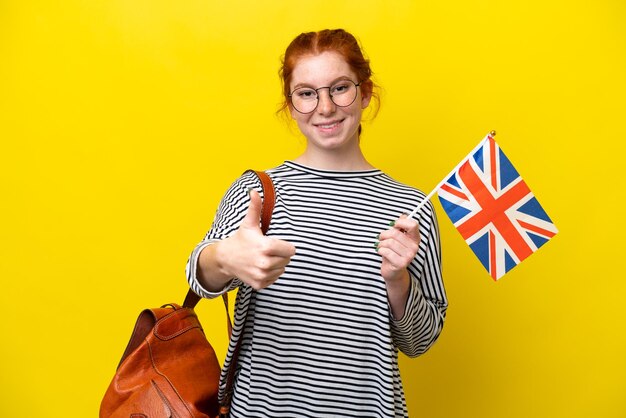 Young hispanic woman holding an united kingdom flag isolated on yellow background with thumbs up because something good has happened