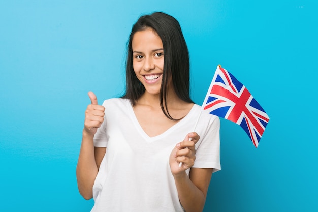 Young hispanic woman holding a united kingdom flag smiling and raising thumb up