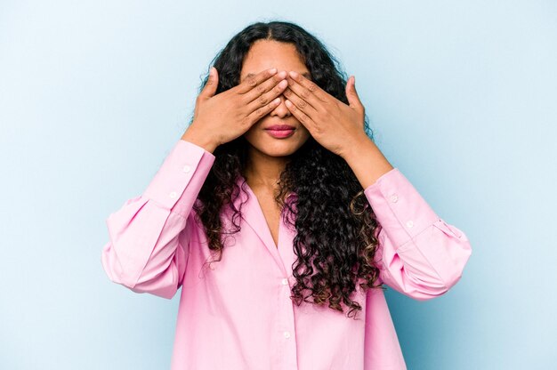 Young hispanic woman isolated on blue background afraid covering eyes with hands