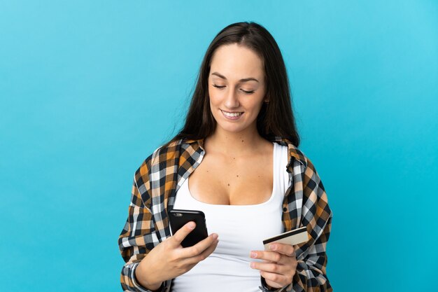 Foto giovane donna ispanica su sfondo blu isolato che acquista con il cellulare con una carta di credito