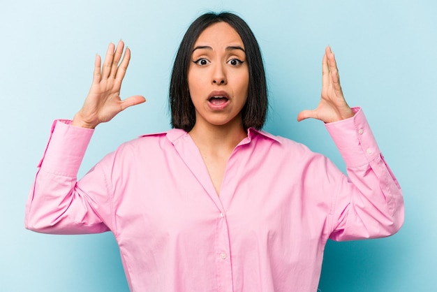 Young hispanic woman isolated on blue background celebrating a victory or success he is surprised and shocked