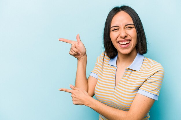 Young hispanic woman isolated on blue background excited pointing with forefingers away