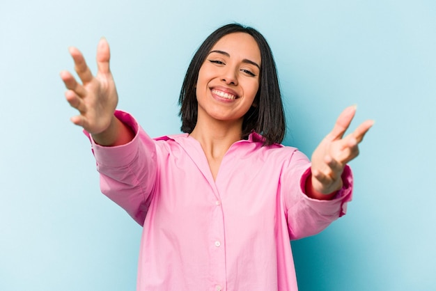 Young hispanic woman isolated on blue background feels confident giving a hug to the camera