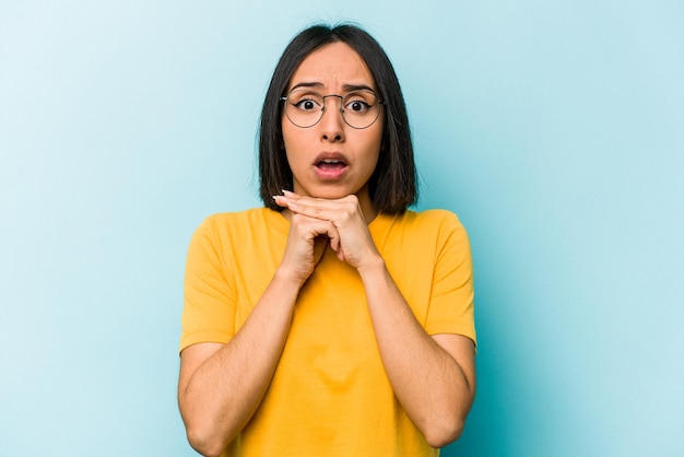 Young hispanic woman isolated on blue background praying for luck amazed and opening mouth looking to front