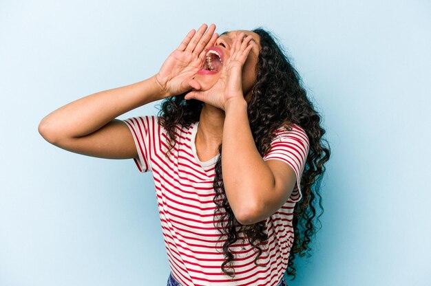 Young hispanic woman isolated on blue background shouting excited to front