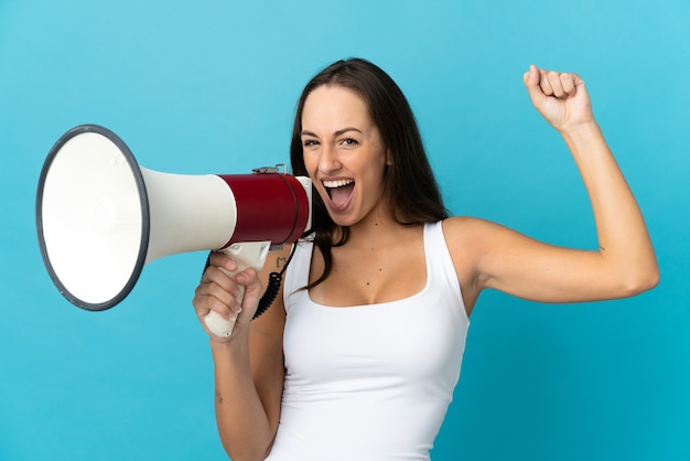 Young hispanic woman over isolated blue background shouting through a megaphone to announce something