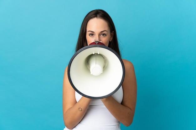 Young hispanic woman over isolated blue background shouting through a megaphone to announce something