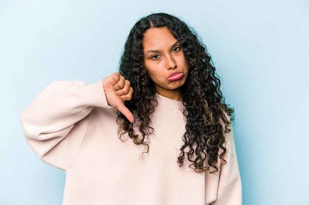 Young hispanic woman isolated on blue background showing a dislike gesture thumbs down Disagreement concept
