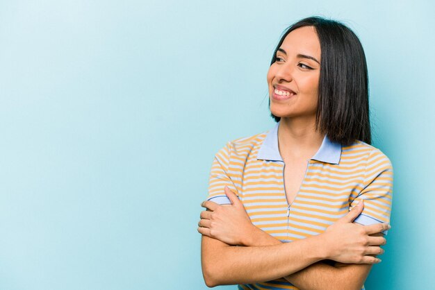 Young hispanic woman isolated on blue background smiling confident with crossed arms