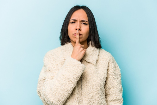 Young hispanic woman isolated on blue background thinking and looking up being reflective contemplating having a fantasy