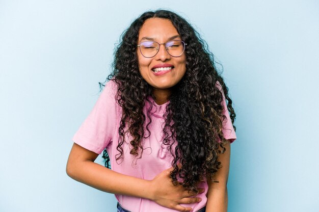 Young hispanic woman isolated on blue background touches tummy smiles gently eating and satisfaction concept