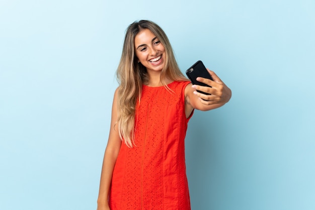 Young hispanic woman over isolated blue wall making a selfie