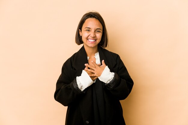 Young hispanic woman isolated laughs happily and has fun keeping hands on stomach.