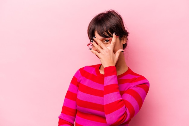 Photo young hispanic woman isolated on pink background blink at the camera through fingers embarrassed covering face