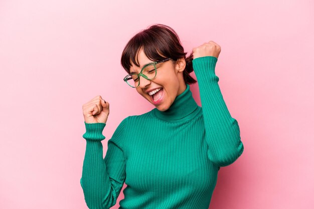 Young hispanic woman isolated on pink background celebrating a special day jumps and raise arms with energy
