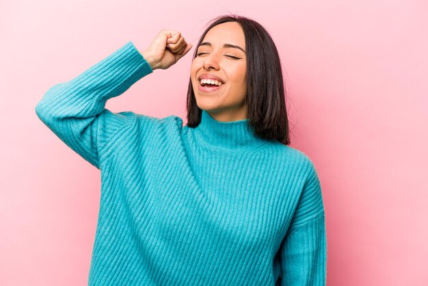 勝利の情熱と熱意の幸せな表現を祝うピンクの背景に分離された若いヒスパニック系女性