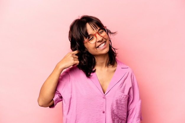 Young hispanic woman isolated on pink background covering ears with hands