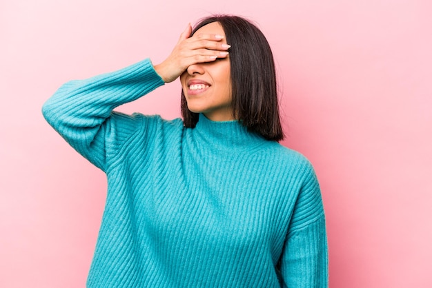 Young hispanic woman isolated on pink background covers eyes with hands smiles broadly waiting for a surprise