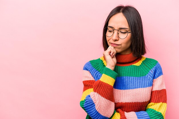 Young hispanic woman isolated on pink background looking sideways with doubtful and skeptical expression