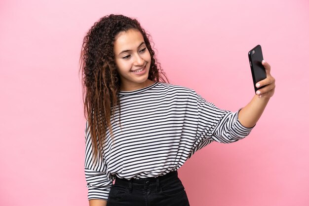 Young hispanic woman isolated on pink background making a selfie