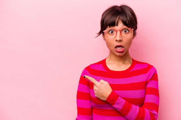 Young hispanic woman isolated on pink background pointing to the side