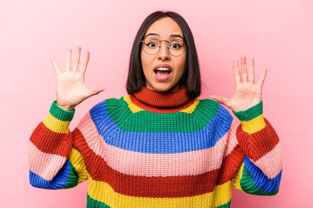 Photo young hispanic woman isolated on pink background receiving a pleasant surprise excited and raising hands