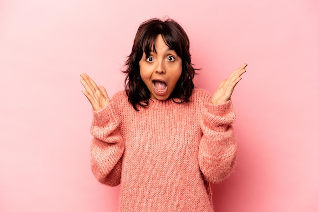 Young hispanic woman isolated on pink background receiving a pleasant surprise excited and raising hands