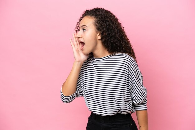 Young hispanic woman isolated on pink background shouting with mouth wide open to the side